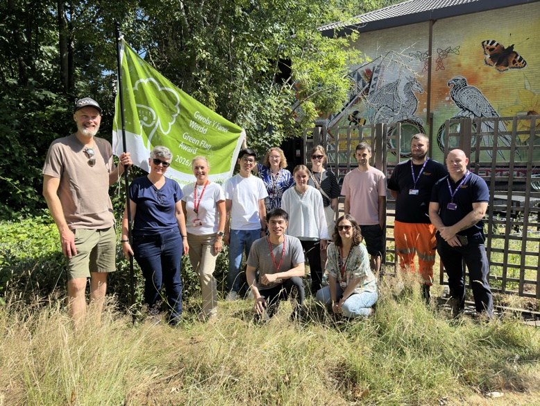 Group of people standing outdoors beside a green biodiversity flag and wildlife mural.