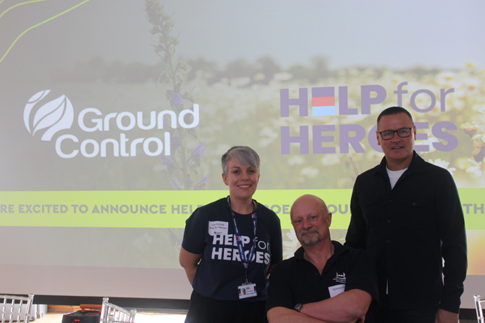 Two individuals from Help for Heroes standing with with Darren Daley, Maintenance & Client Services Director, in front of both company logos