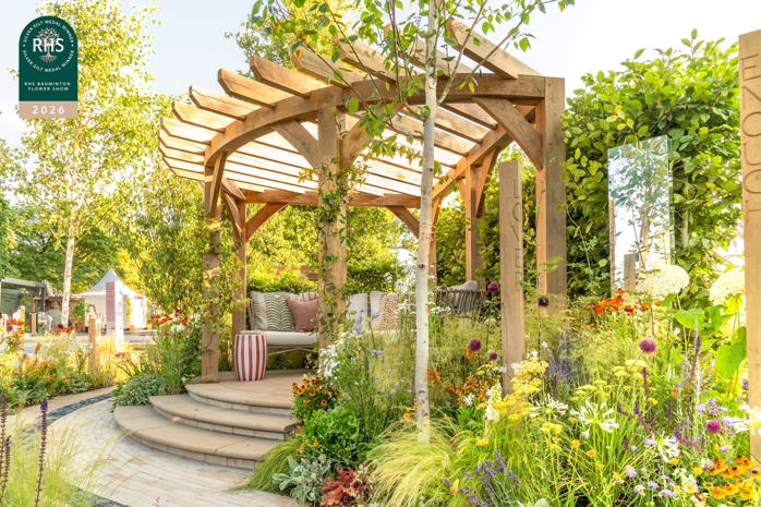 Wooden garden pergola surrounded by colourful flowers and planting with outdoor seating beneath.